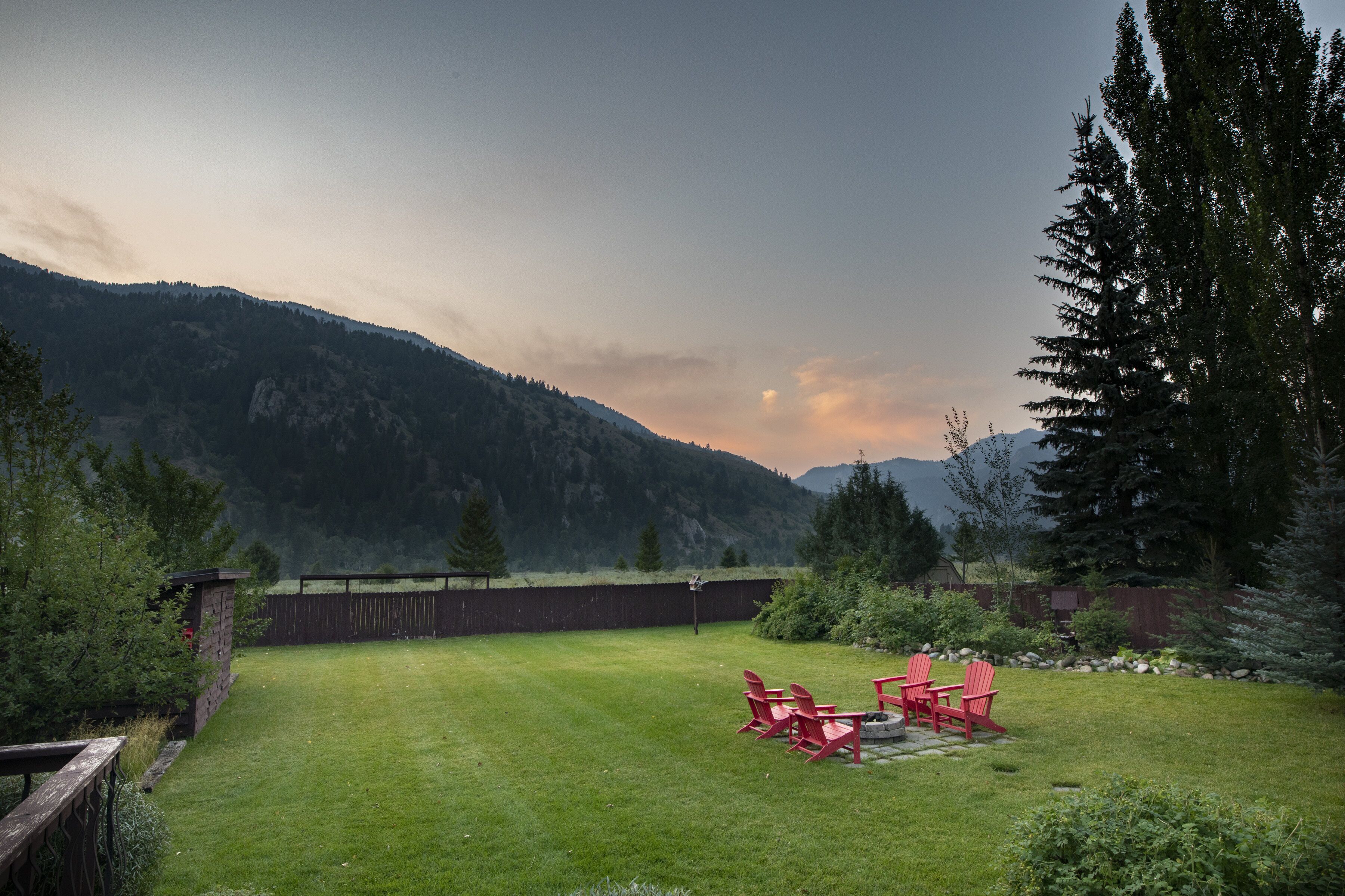 Un jardin avec une pelouse verdoyante, une terrasse en bois et un fauteuil Adirondack rouge.