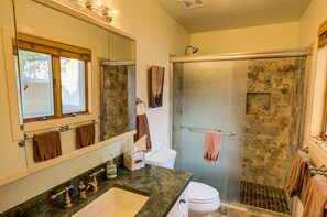 A bathroom with a stone shower enclosure, a white toilet, a sink with a marble countertop, and a large mirror.