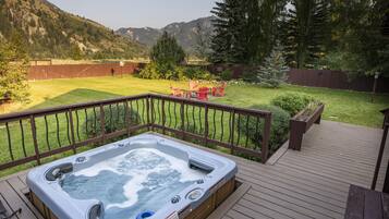 A hot tub on a wooden deck with a view of a grassy yard and mountains in the background.