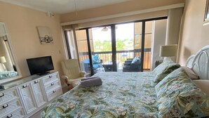 A bedroom with a bed, a television, a dresser, and a balcony with outdoor furniture. - The CHART ROOM -with off the chart views!! (Burnt Store Marina)