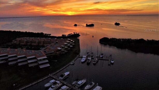 A marina with boats docked, a building complex with multiple levels, and a sunset over the water. - The CHART ROOM -with off the chart views!! (Burnt Store Marina)