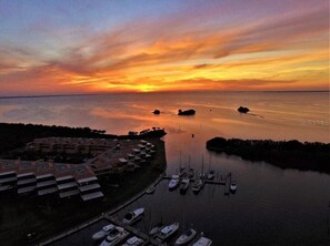 A marina with boats docked, a building complex with multiple levels, and a sunset over the water. - The CHART ROOM -with off the chart views!! (Burnt Store Marina)