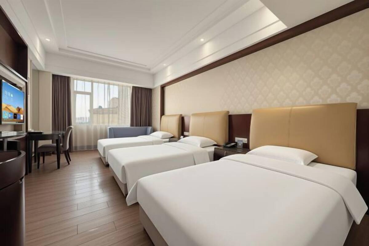A hotel room with three beds, a desk, a TV, and a window with curtains.