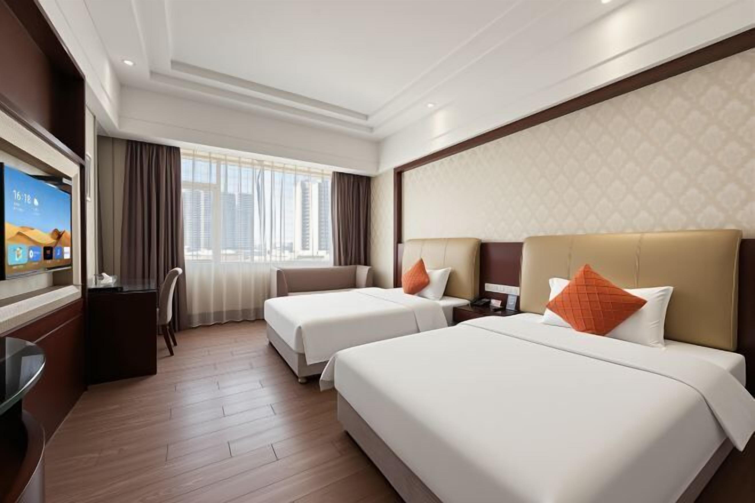 Une chambre d’hôtel avec deux lits, un bureau, une télévision et une grande fenêtre avec des rideaux.