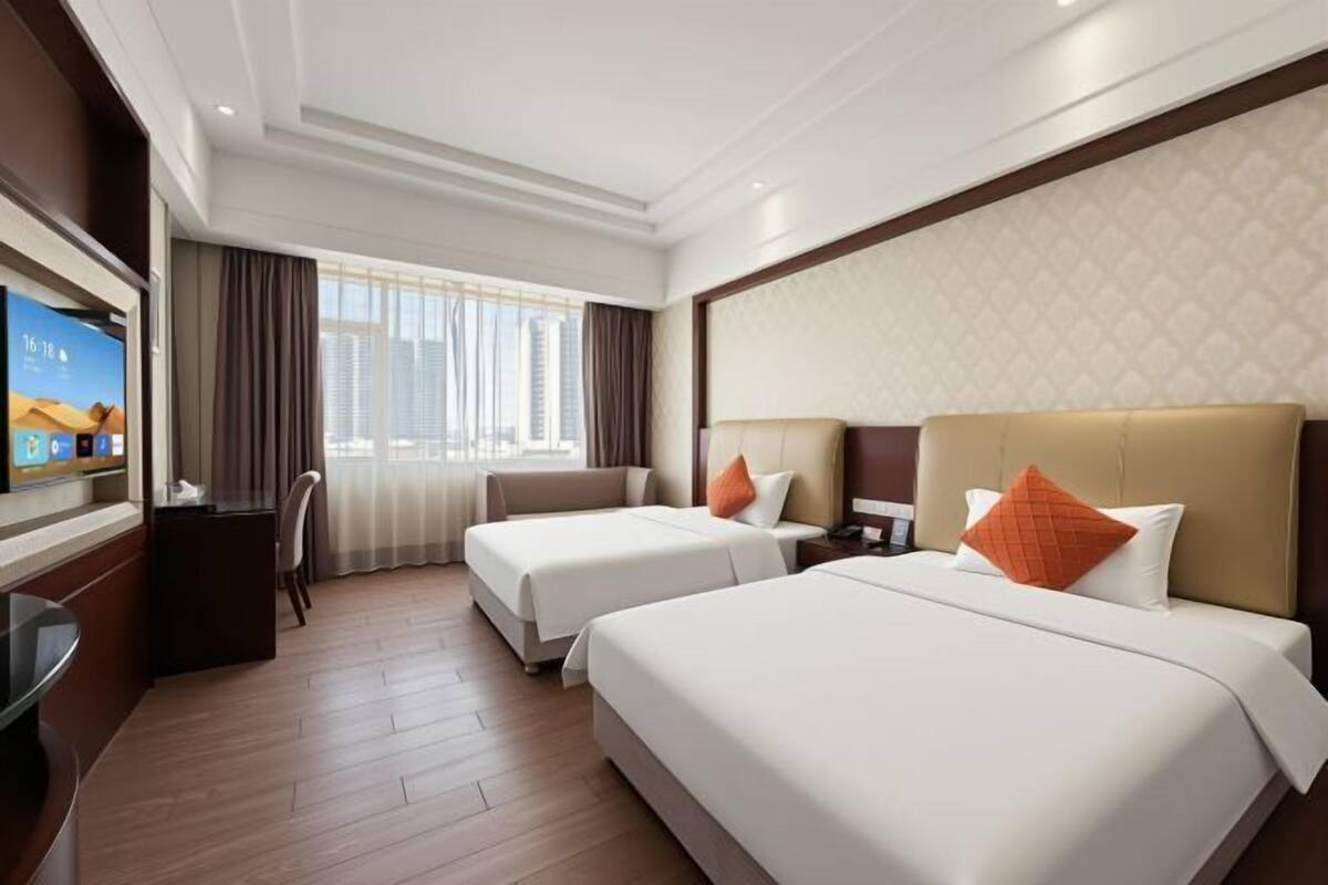 A hotel room with two beds, a desk, a TV, and a large window with curtains.