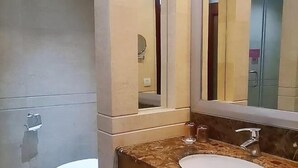 Un baño con lavamanos de mármol, un espejo y un inodoro.