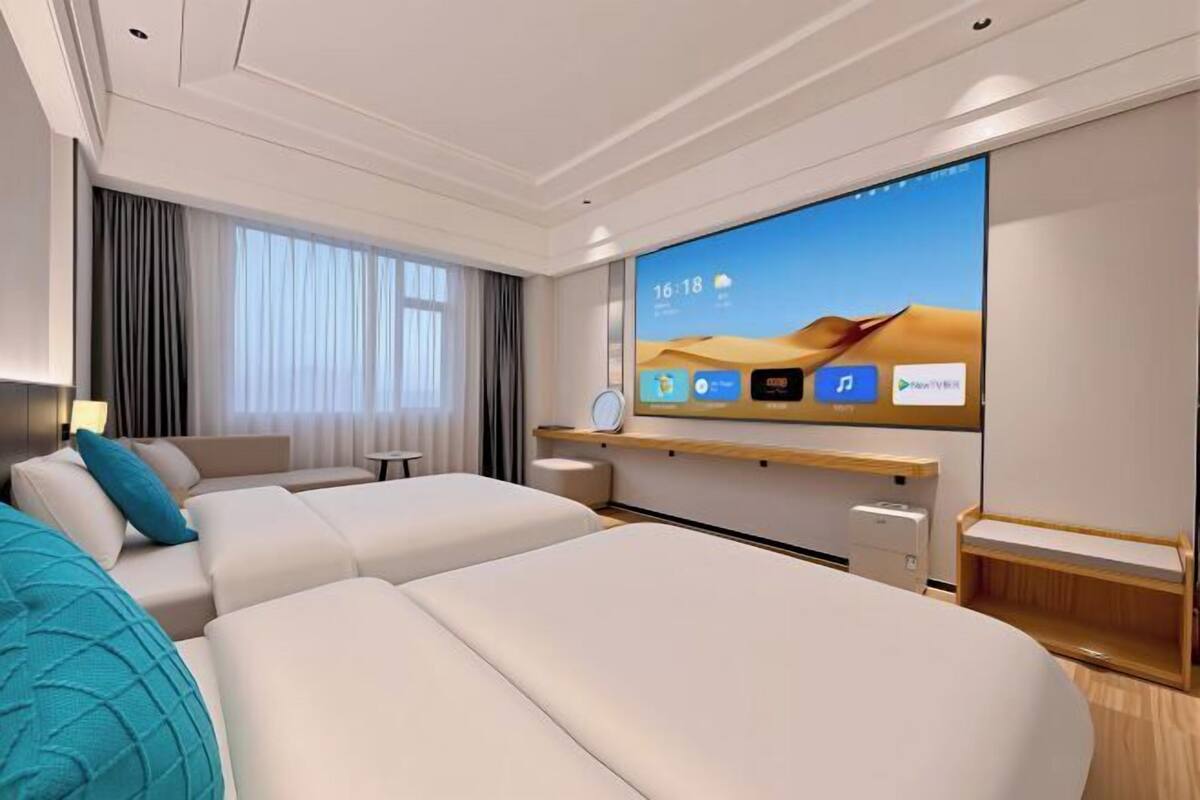 A modern hotel room with a large bed, a TV, a desk with a computer, and a window with curtains.