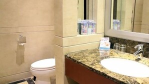Un baño con inodoro, lavamanos, espejo y artículos de aseo en la encimera.