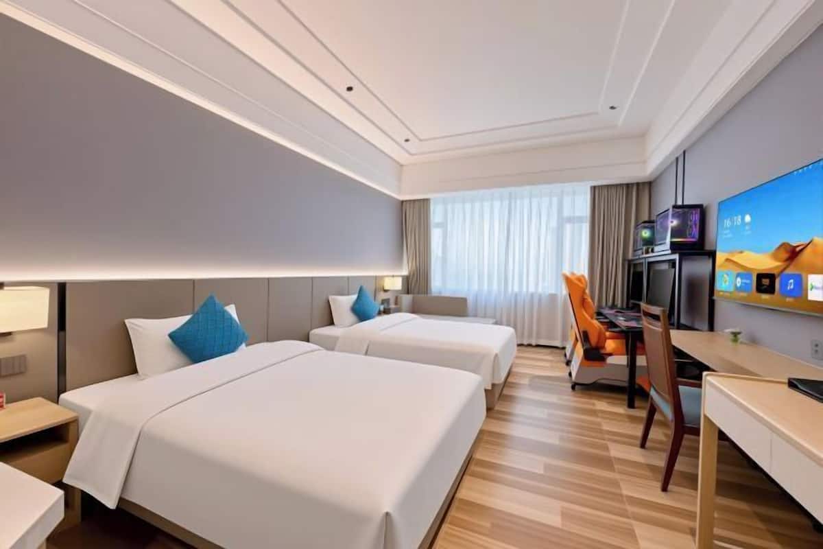 A hotel room with two beds, a desk, a TV, and a window with curtains.