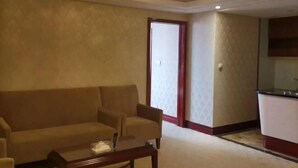 Una sala de estar con un sofá, sillones y una mesa de centro. Hay una puerta que conduce a otra habitación y una pequeña zona de cocina con un fregadero.