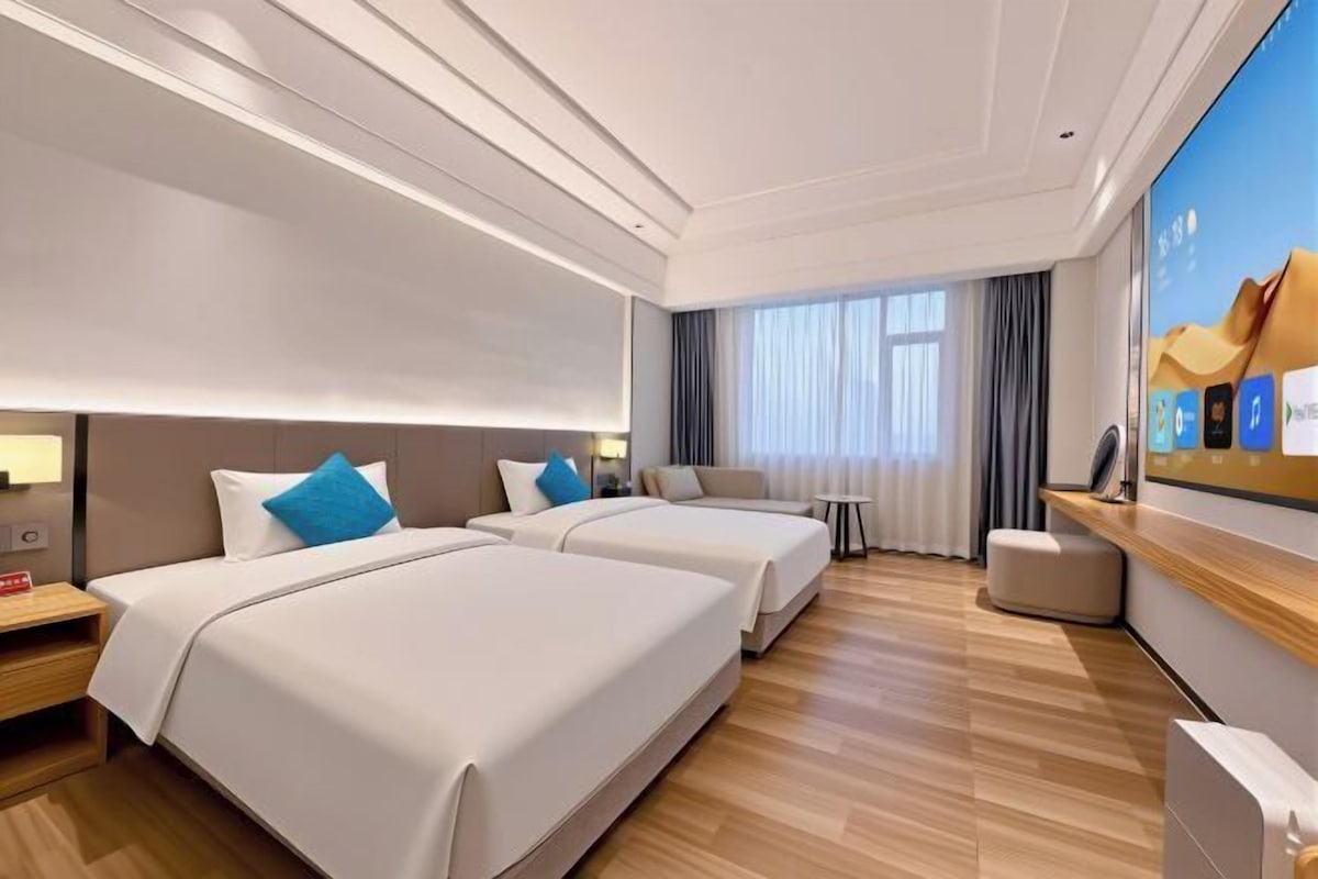 A hotel room with two beds, a TV, a desk, and a window with curtains.