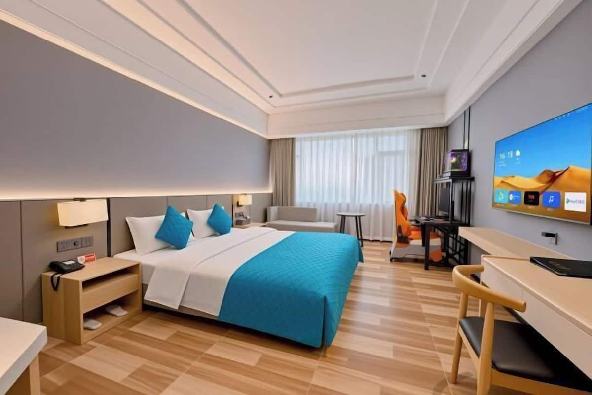 A hotel room with a bed, desk, chair, TV, and a window with curtains.
