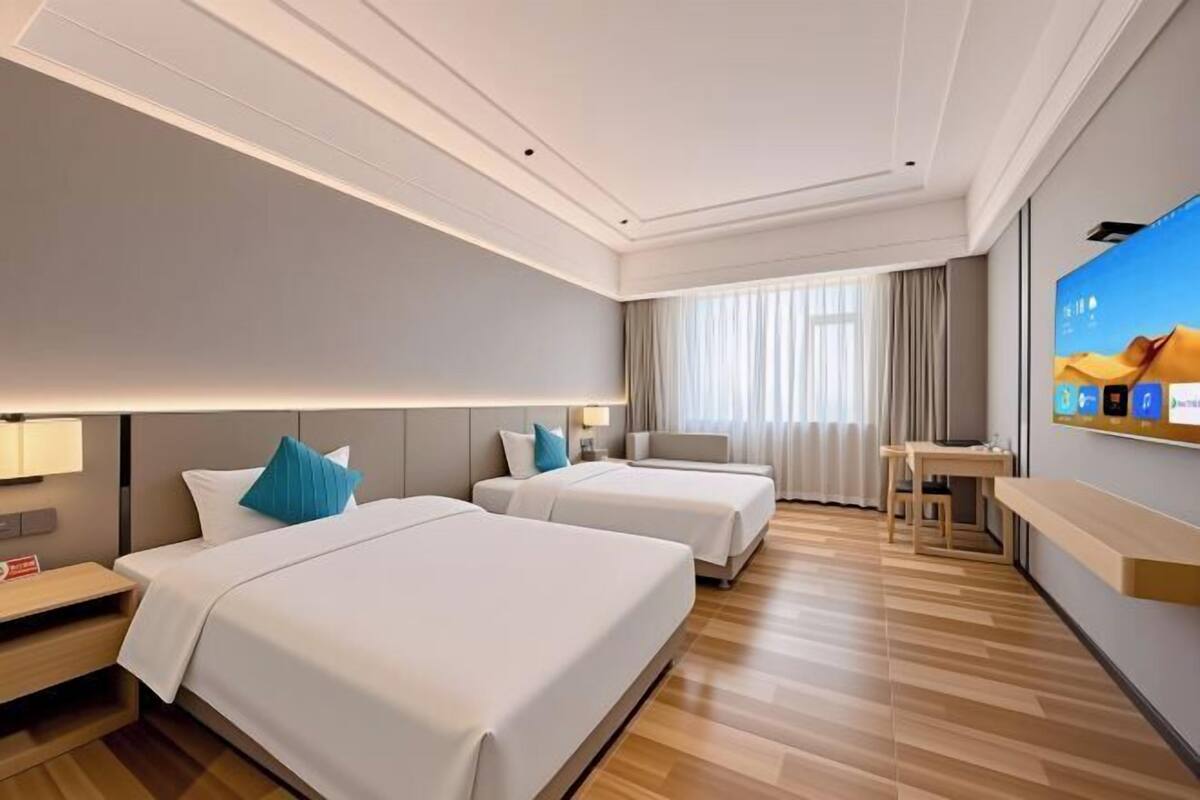A hotel room with two beds, a desk, a TV, and a window with curtains.