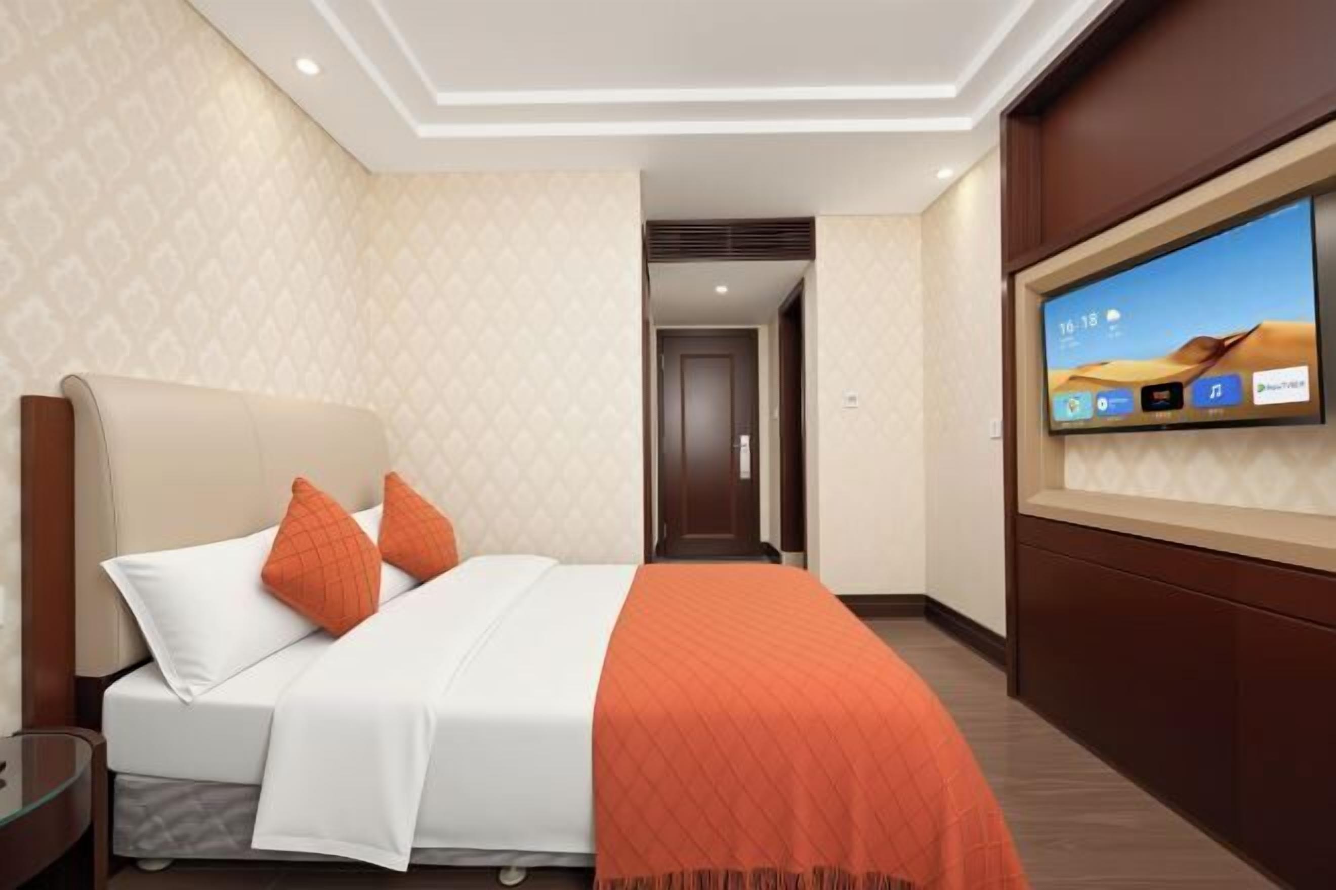 Une chambre d’hôtel avec un lit, un téléviseur fixé au mur et une porte donnant sur une autre pièce.