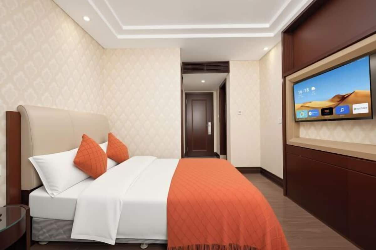 A hotel room with a bed, a TV on the wall, and a door leading to another room.