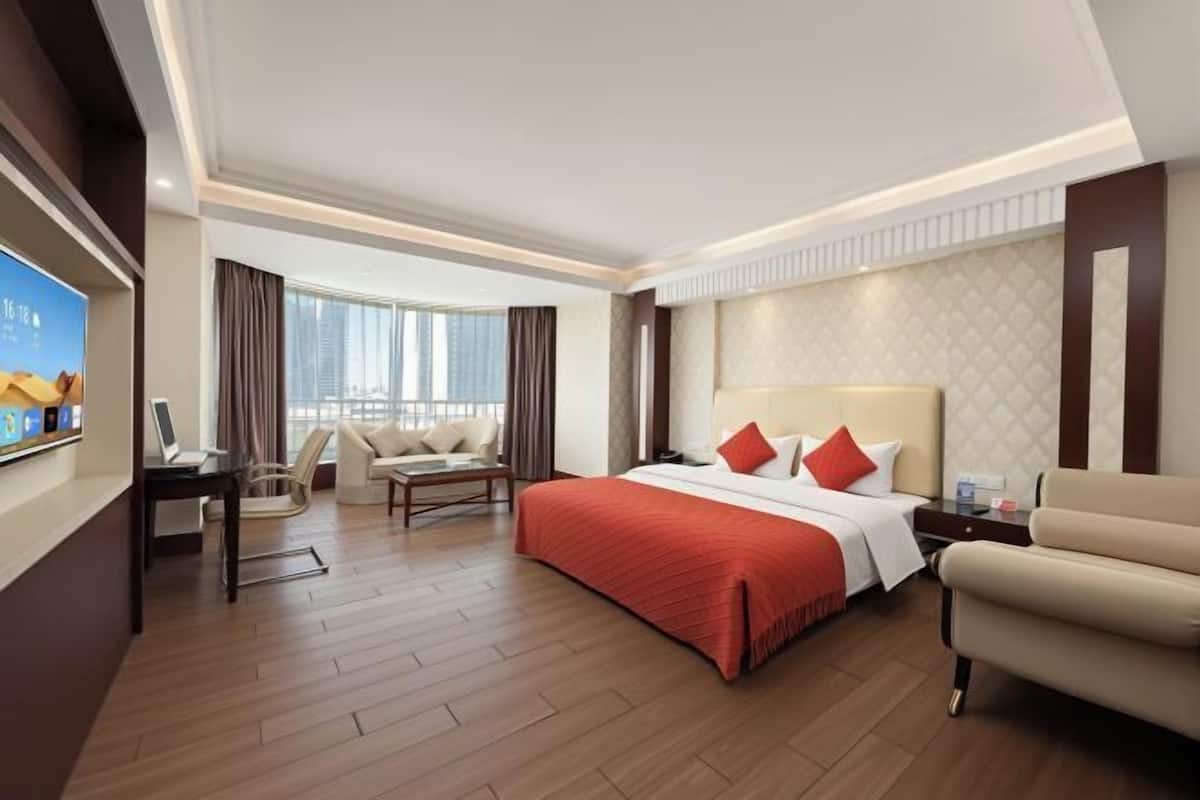 A hotel room with a large bed, a desk, a chair, a sofa, and a TV.