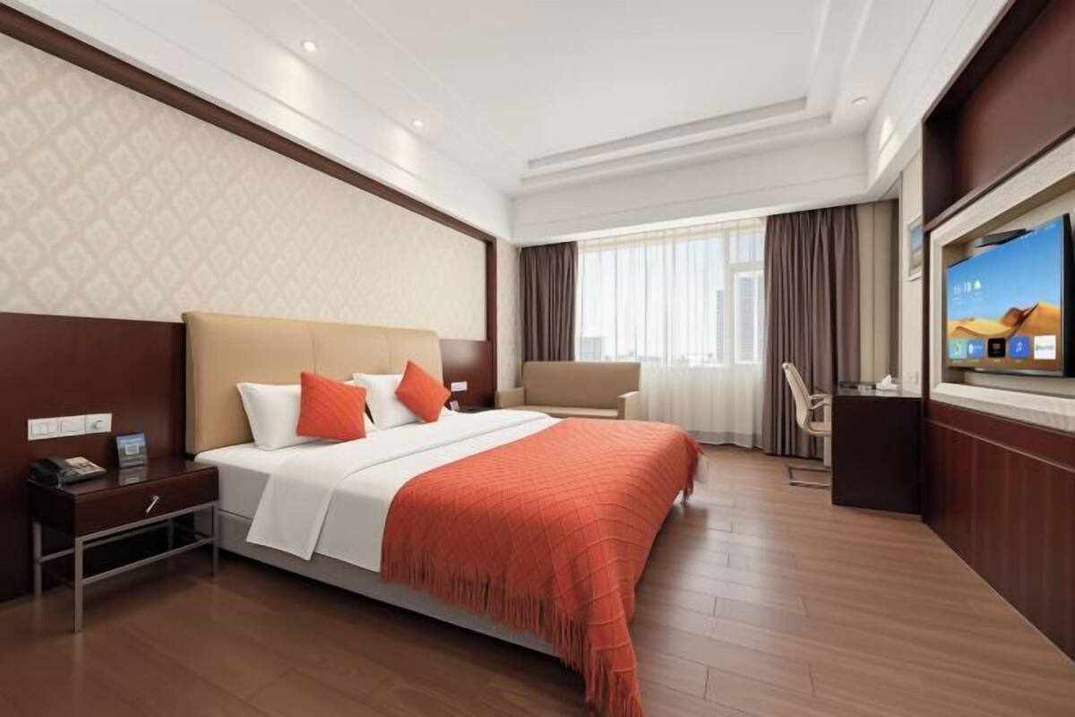 A hotel room with a large bed, a TV, a desk, and a window with curtains.