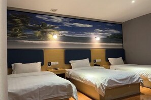 Une chambre d’hôtel avec trois lits, une grande fresque murale sur le thème de la plage et une tête de lit en bois.