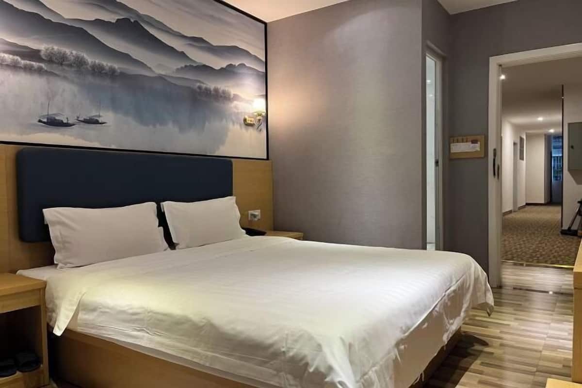 A hotel room with a large bed, a nightstand, a wall-mounted painting, and a door leading to another room.