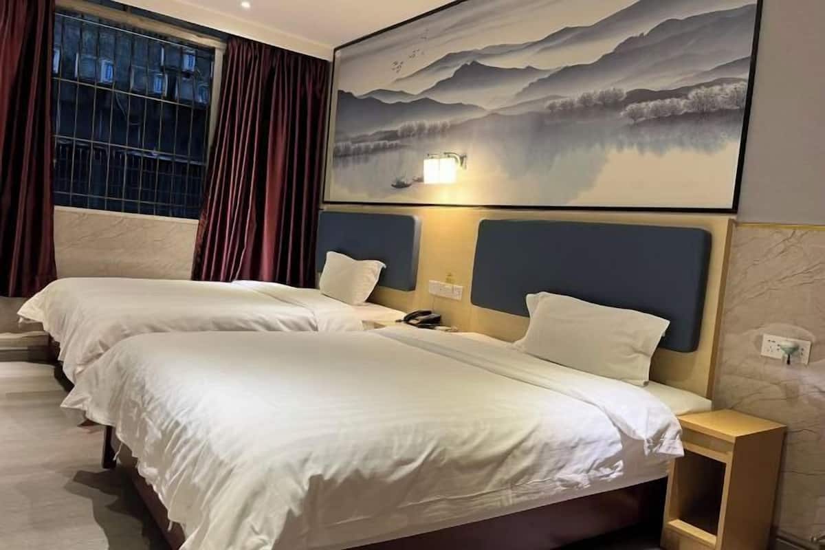A hotel room with two beds, a painting of mountains, a night light, and a window with curtains.