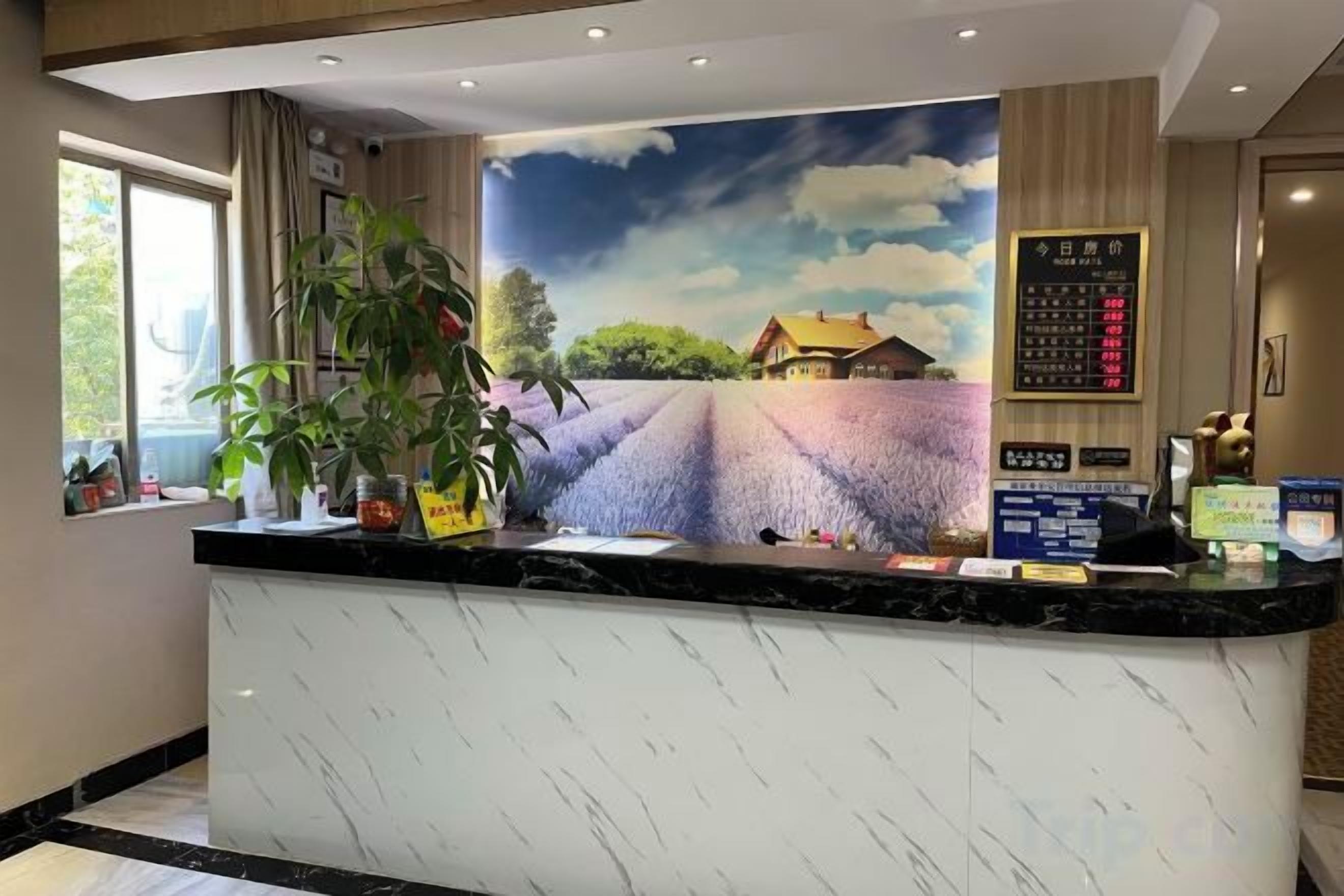 A reception desk with a large mural of a lavender field, a digital display board, and a potted plant.