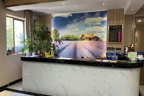 Mostrador de recepción con un gran mural de un campo de lavanda, un tablero de anuncios digital y una planta en maceta.