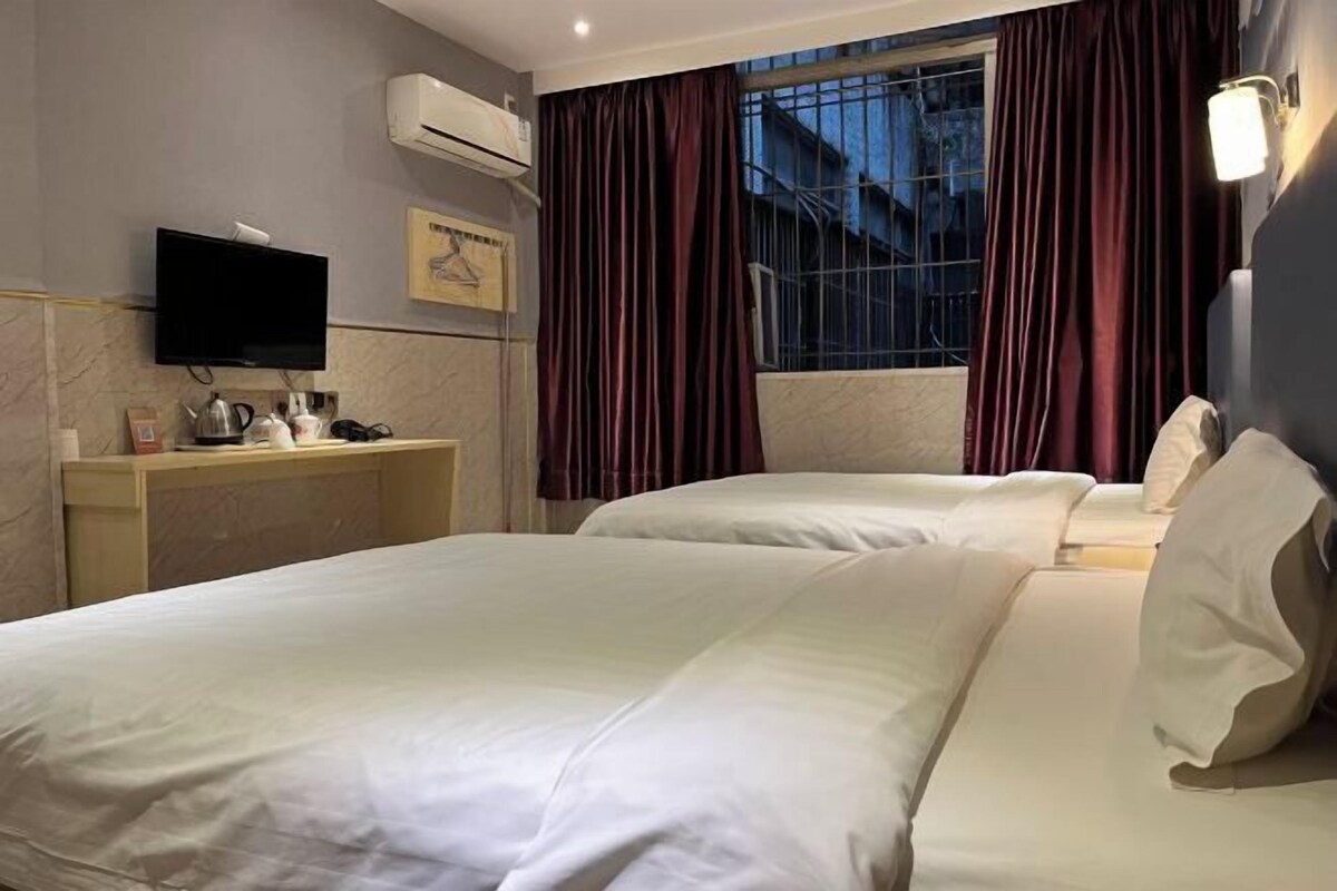 A hotel room with two beds, a TV, a desk with a kettle, and a window with curtains.