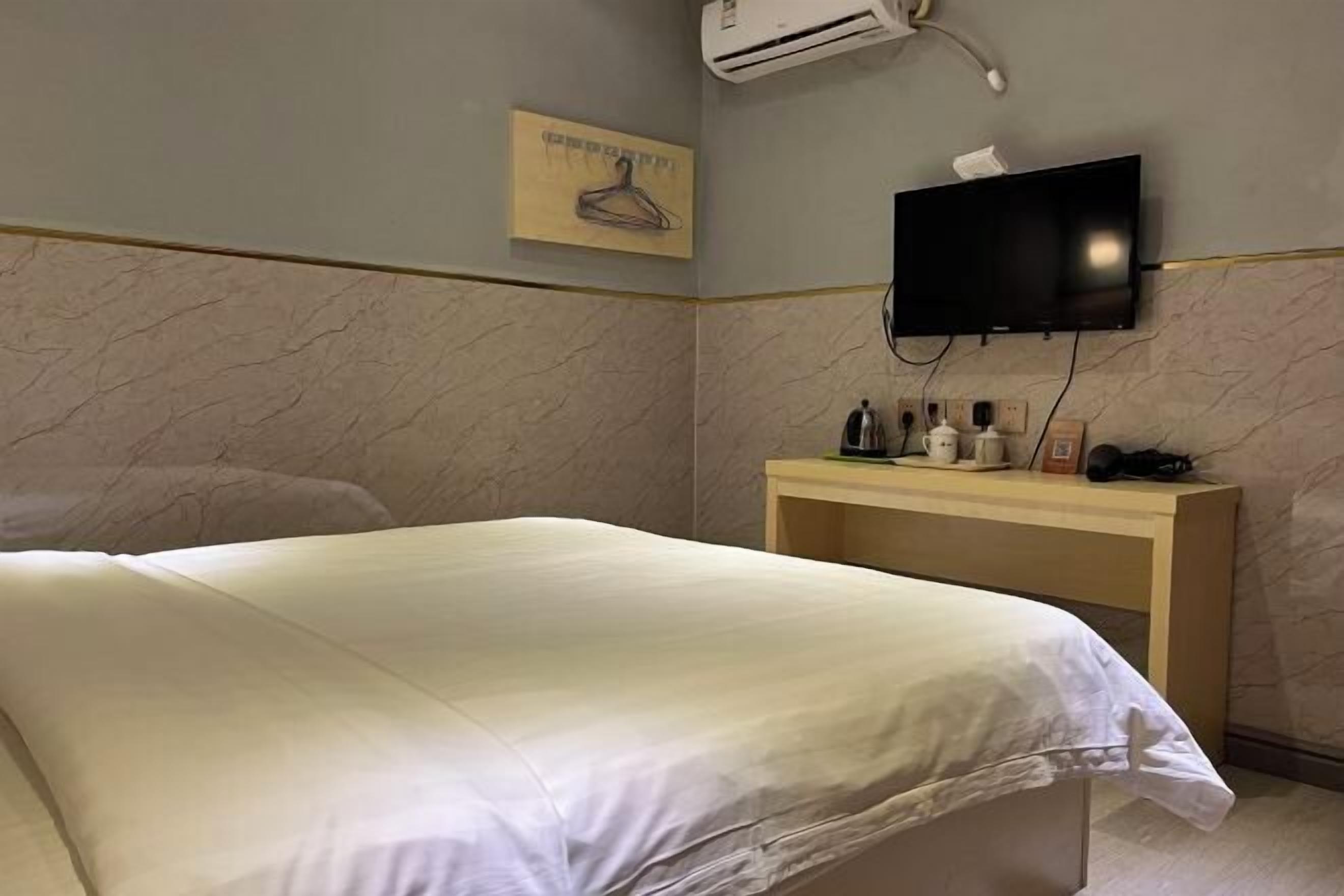 Une chambre d’hôtel comprenant un lit, un téléviseur fixé au mur, une console en bois avec des articles de toilette et un climatiseur mural.