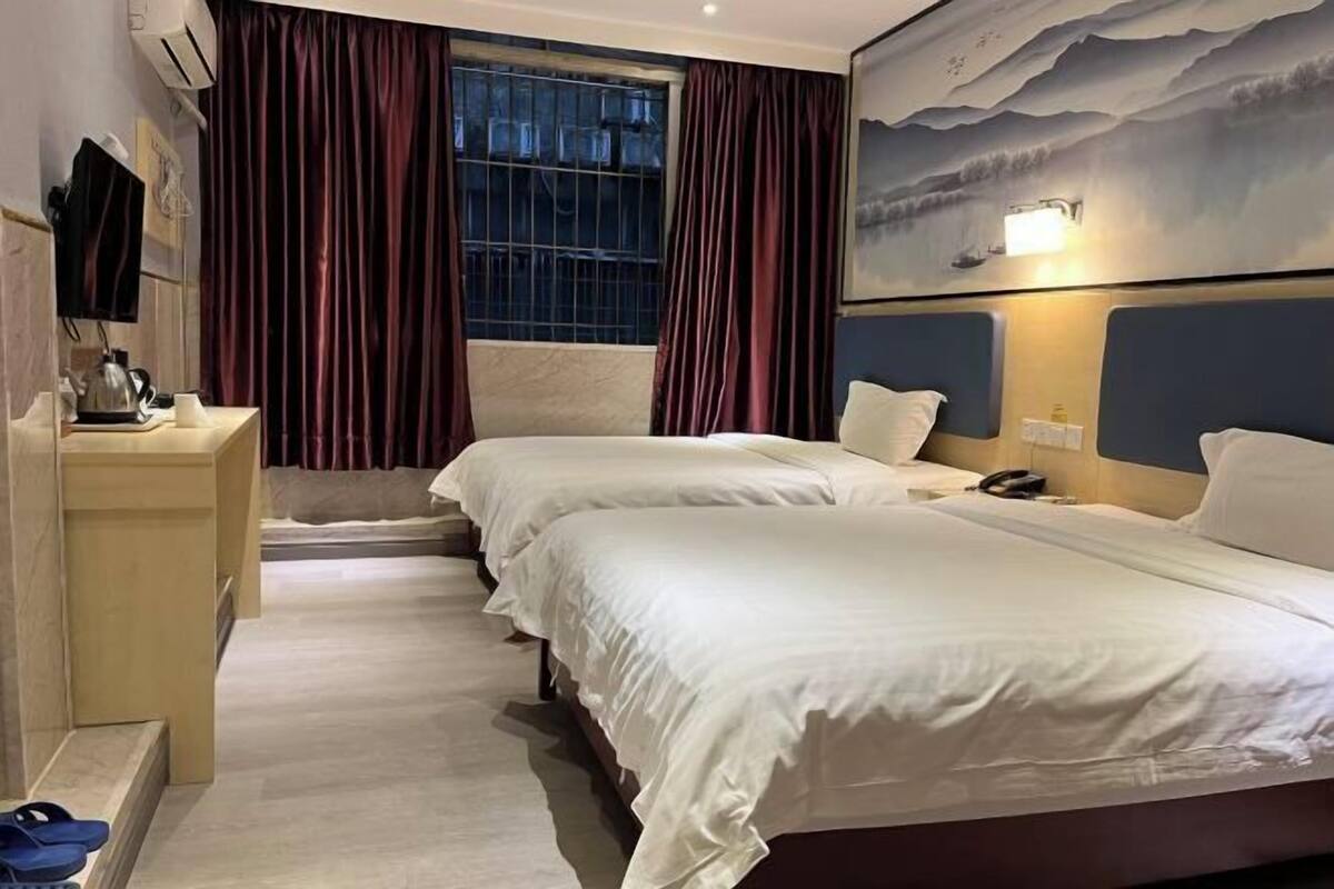 A hotel room with two beds, a desk, a chair, a TV, and a painting on the wall.