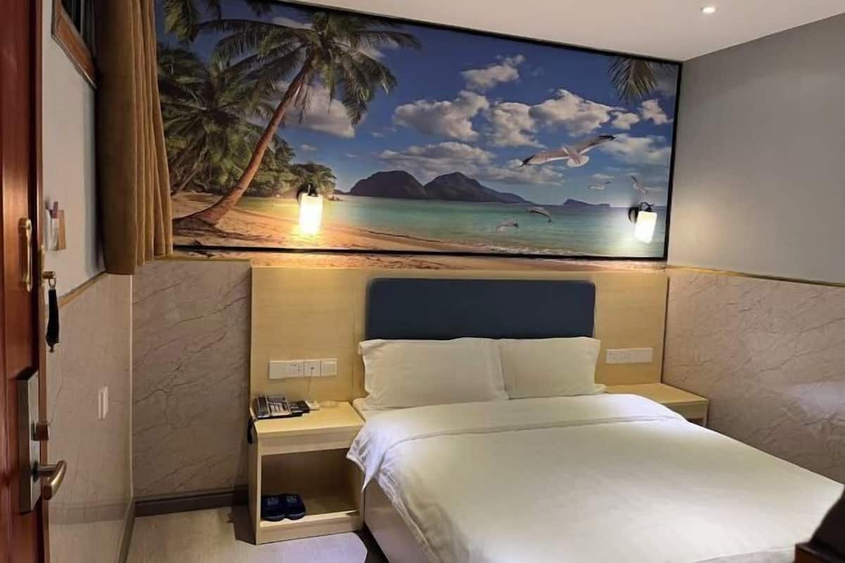 A hotel room with a bed, nightstands, a painting of a beach scene, and a door.