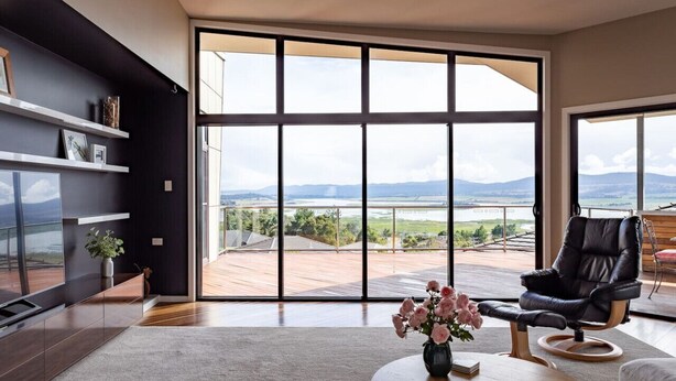 A modern living room with a large sliding glass door leading to a deck, a black leather chair, and a vase of flowers on a coffee table.