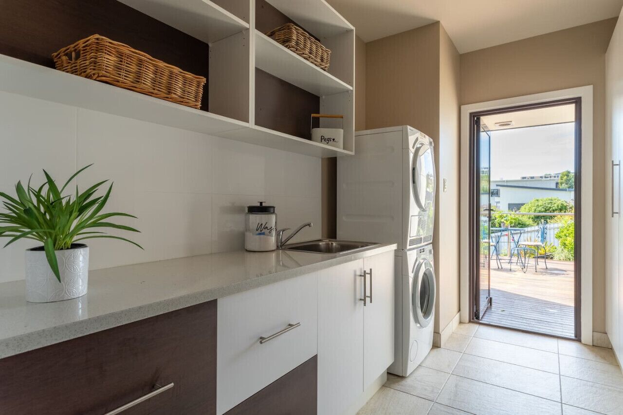 A modern kitchen with white cabinets, a built-in washing machine, and a potted plant.