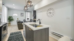 A modern kitchen with a central island, pendant lights, and a large wall clock. - Modern Niagara-area Spa-like Home (St. Catharines)