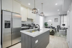 Une cuisine moderne dotée d’un îlot central, d’appareils électroménagers en acier inoxydable et de luminaires suspendus.
