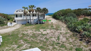 A beachfront house with a covered porch, palm trees, and a sandy path leading to the ocean. - Melbourne Beach House and Basement Apt on 1.2 acres ocean front (Melbourne Beach)