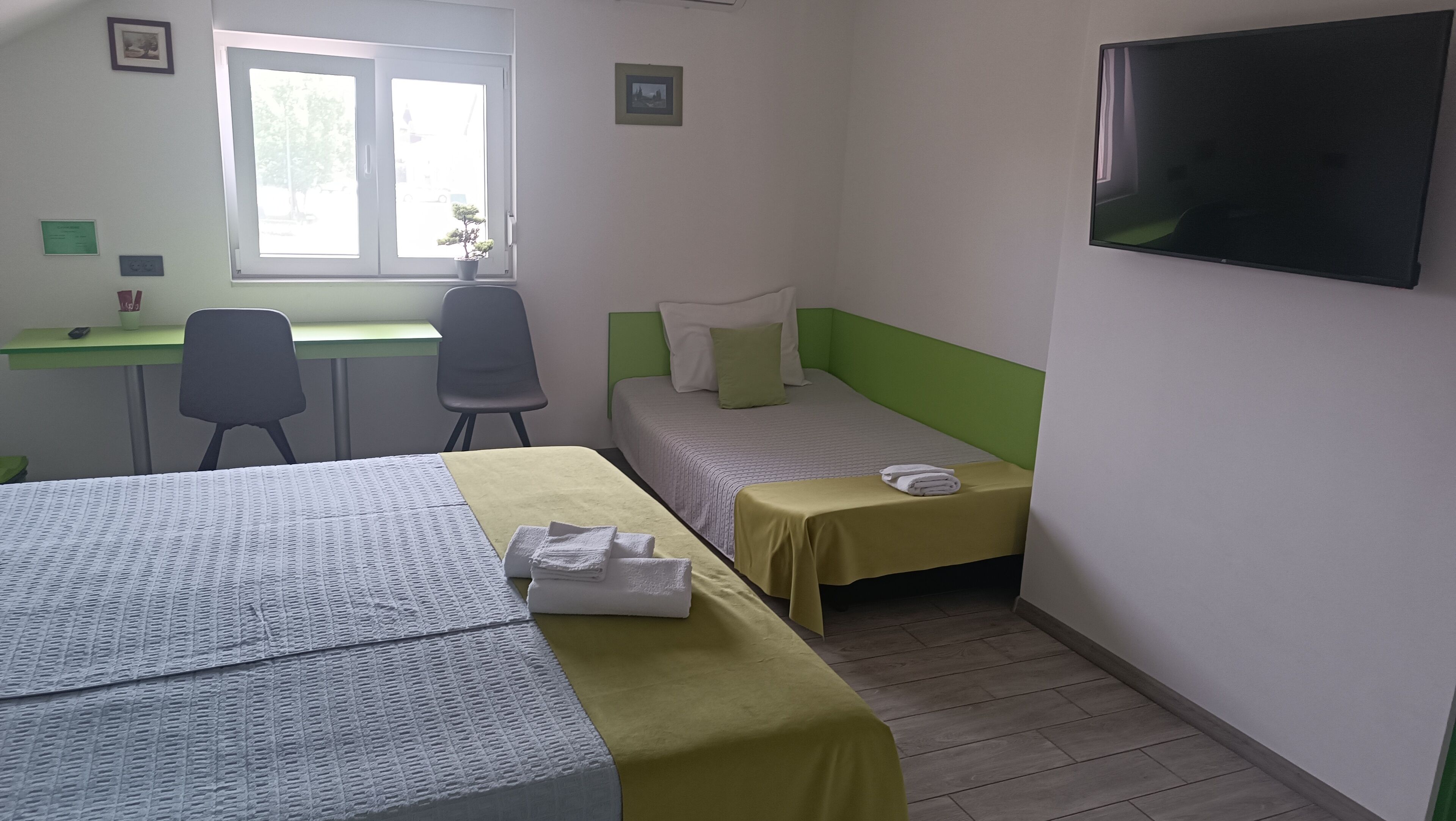 Una habitación de hotel con dos camas, un escritorio, una silla, un televisor y una ventana.