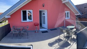 Un edificio con techo rojo y un patio cubierto con mesas y sillas al aire libre, y una puerta.