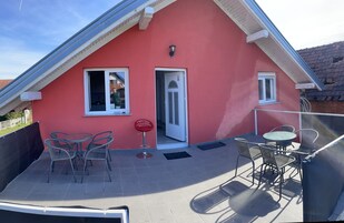 Un edificio con techo rojo y un patio cubierto con mesas y sillas al aire libre, y una puerta.