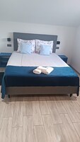Una cama bien hecha con una colcha azul, dos almohadas con motivos florales y una pila de toallas dobladas sobre la cama.