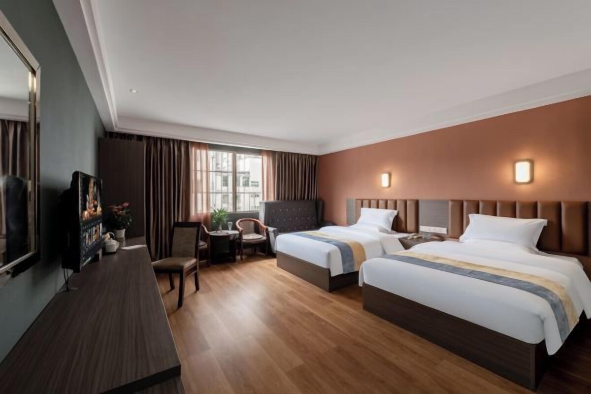A hotel room with two beds, a desk, a chair, and a television.