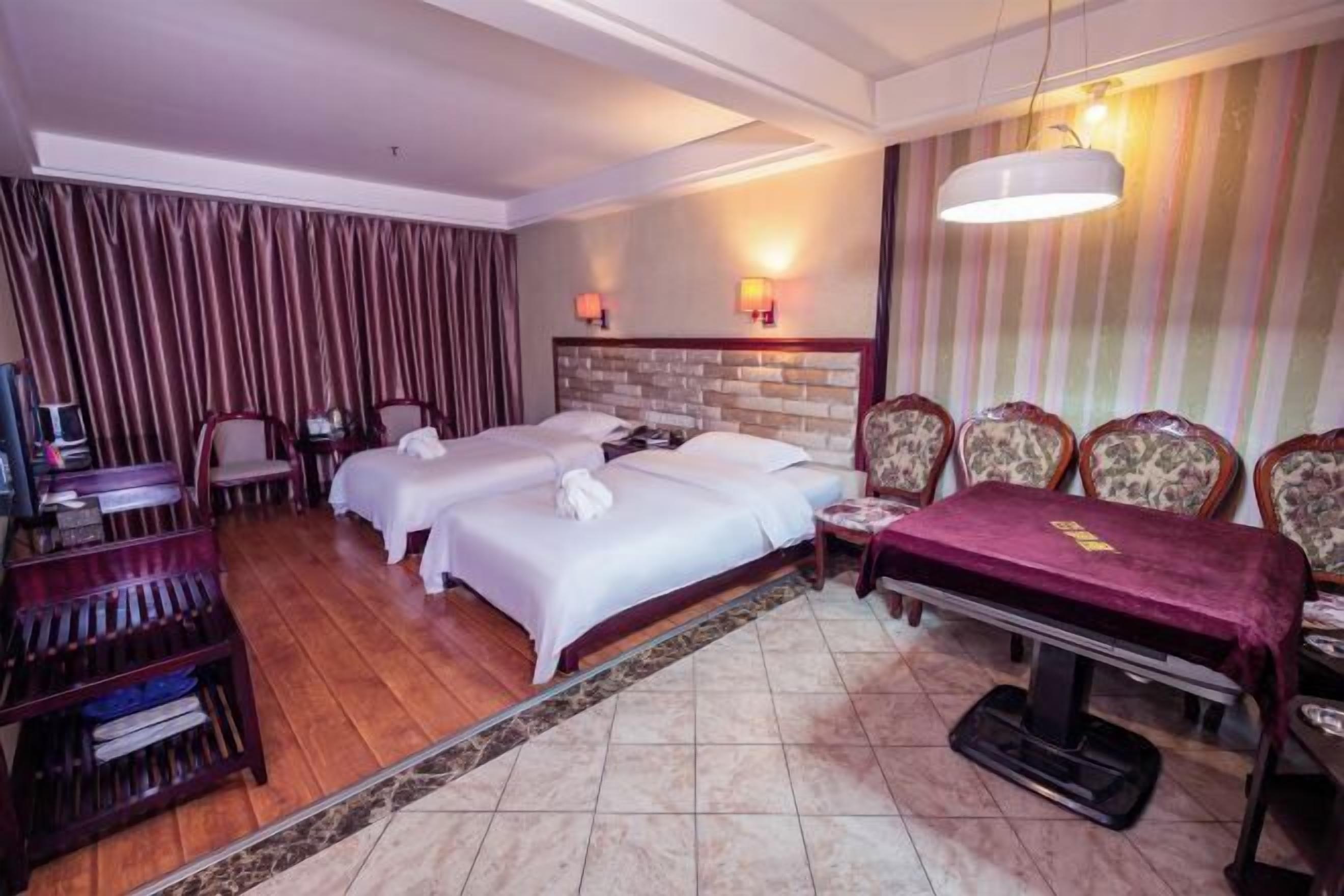 A hotel room with two beds, a desk, a chair, a TV, and a dining table with a red tablecloth.
