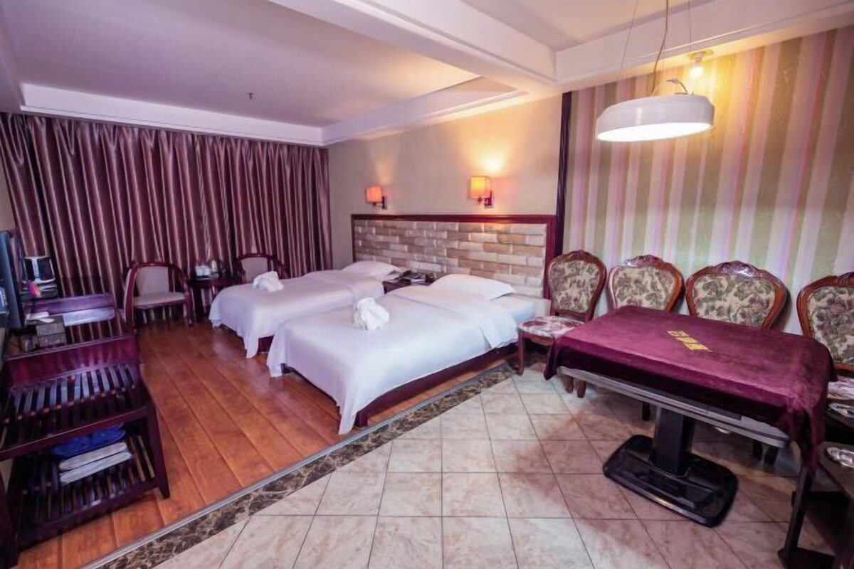 Une chambre d’hôtel avec deux lits, un bureau, une chaise, une télévision et une table à manger recouverte d’une nappe rouge.