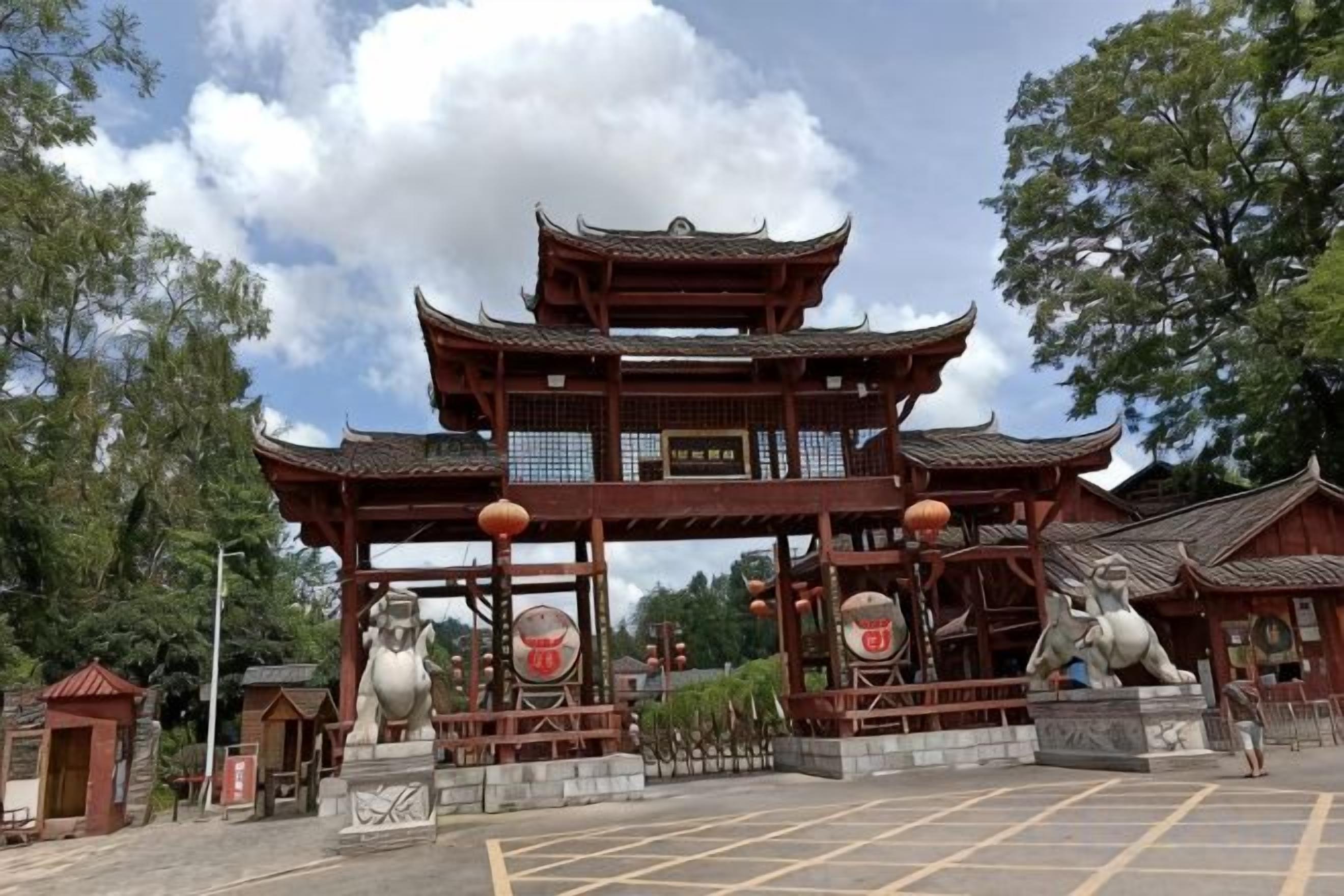 A traditional Chinese gate with multiple tiers and ornate decorations, surrounded by statues and a parking area.
