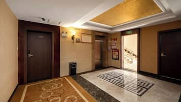 Um hall de hotel com piso coberto por carpete, um balcão de recepção e uma escadaria para um andar superior.