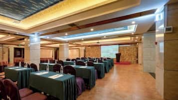 A conference room with rows of tables and chairs, a podium, and a large screen.