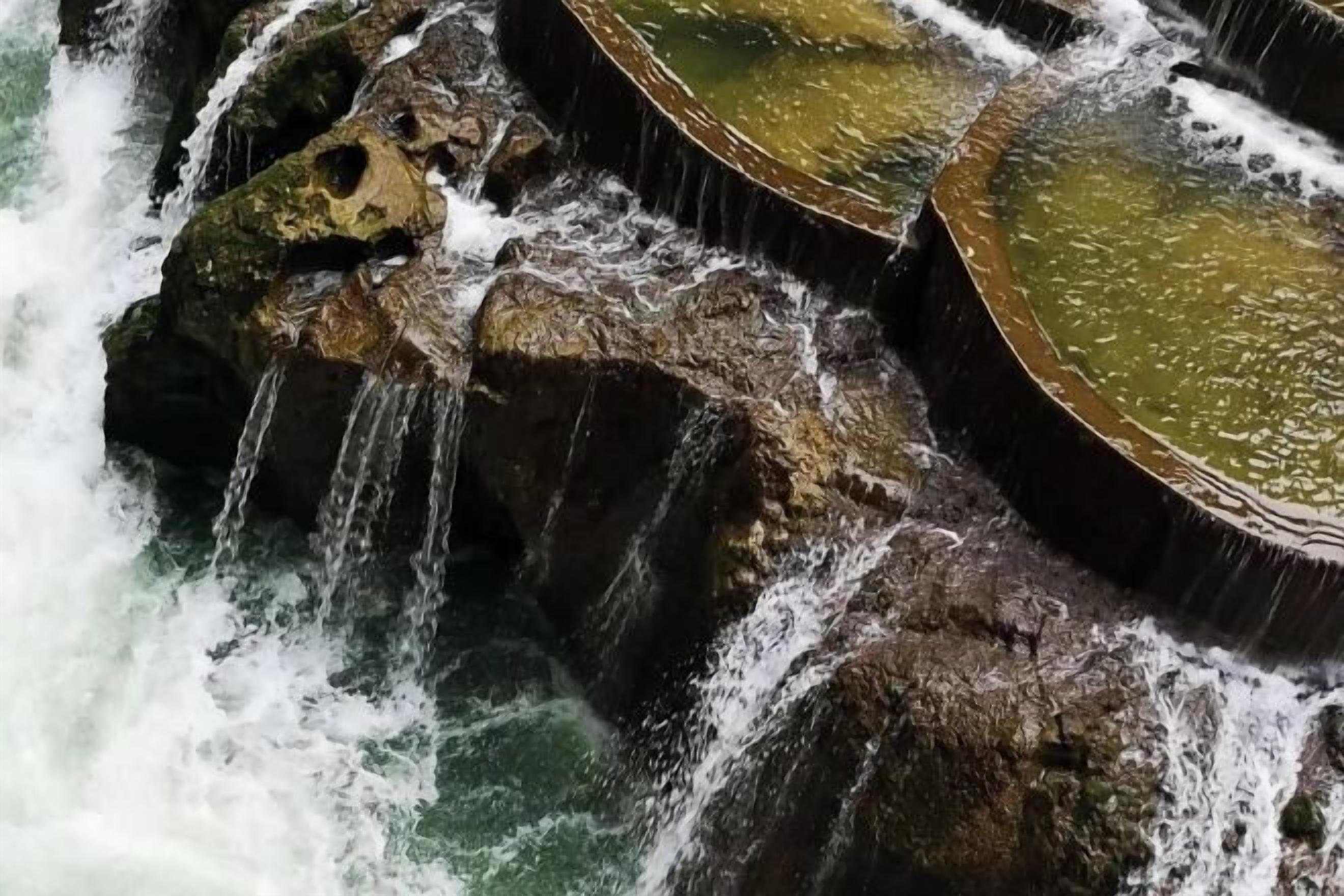 A natural water feature with cascading water over rocks and into a pool.