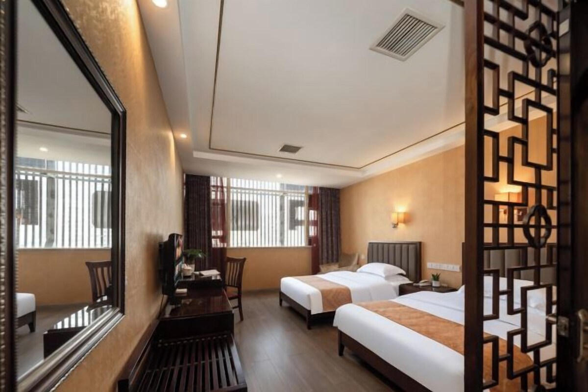 A hotel room with two beds, a desk, a chair, and a large mirror.