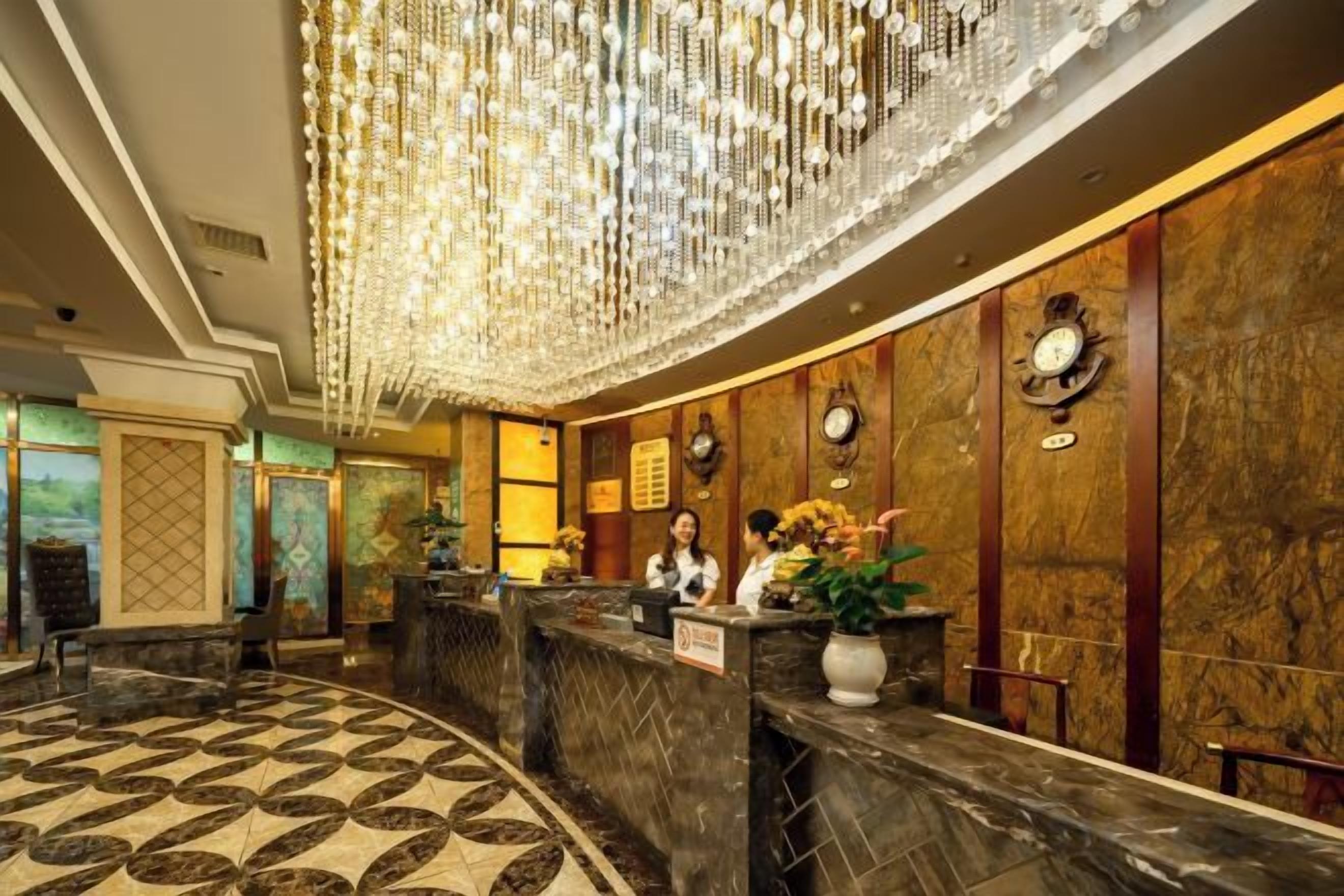 A hotel reception area with a marble floor, a chandelier, and a reception desk.