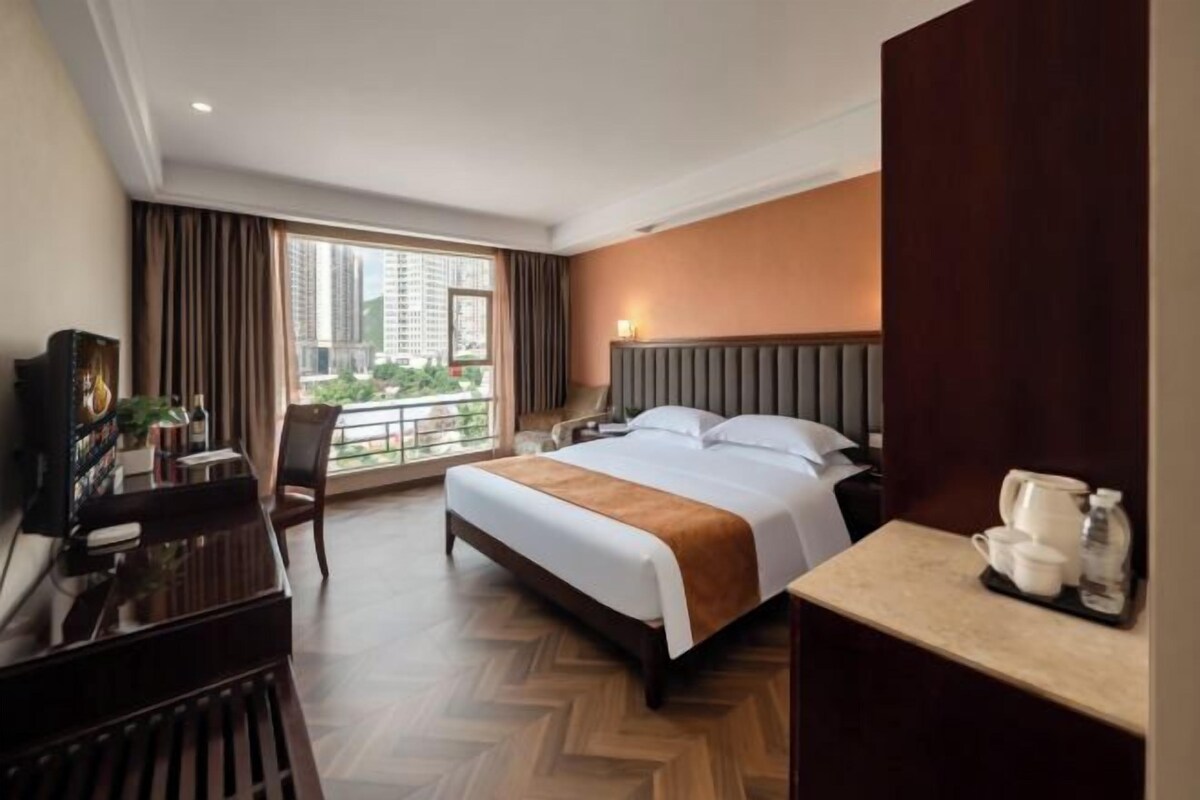 A hotel room with a large bed, a desk with a chair, a nightstand, and a view of the outdoors.