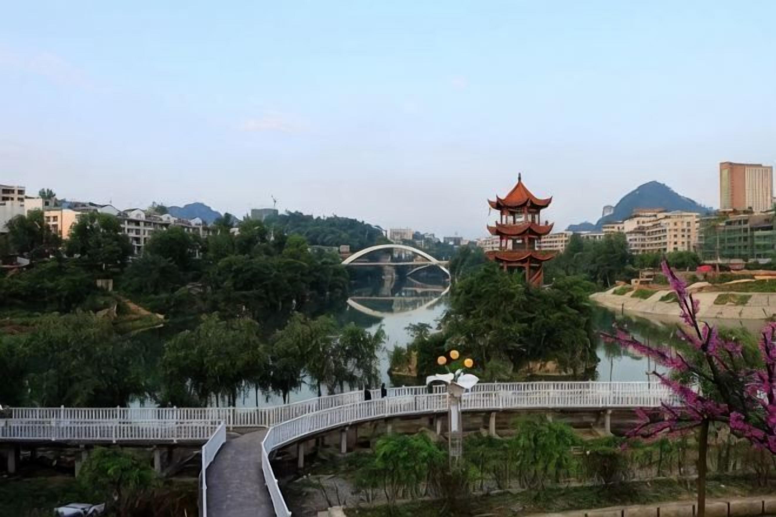 A bridge with a white railing, a pagoda, and a river with trees.